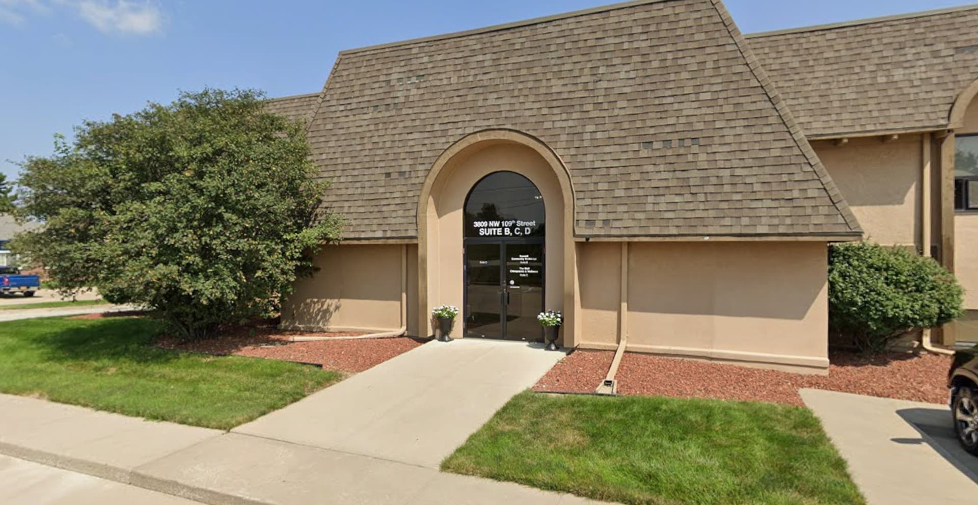Street view of the Urbandale office entrance at 3809 NW 109th Street, Suites B, C, and D—a welcoming tan building with landscaped walkway.